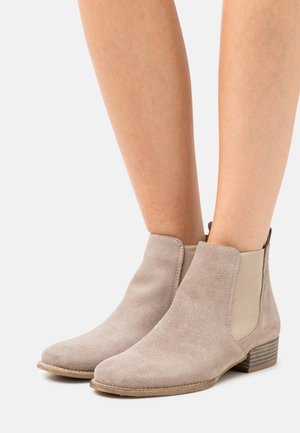 Beige Wildleder-Stiefeletten mit elastischen Seiteneinsätzen, runder Zehenpartie und niedrigem, gestapeltem Absatz. Glatte Textur und minimalistisches Design.