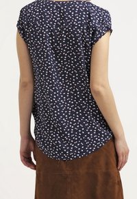 Blusa blu navy a maniche corte con un motivo floreale di piccoli fiori bianchi e rosa, orlo curvo e tessuto morbido.