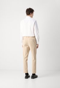 Beige bombažna hlače s krojem, ki se prilega, z ravnim sprednjim delom in zadnjimi žepi, v kombinaciji z belo srajco z dolgimi rokavi in črnimi čevlji.