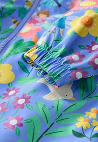 Barevná dětská nepromokavá bunda s modrým květinovým vzorem, elastickými manžetami a ilustracemi květin, ptáků a postaviček.