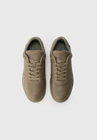 Sneakers in pelle verde con punta rotonda, chiusura con lacci, colletto imbottito e dettagli testurizzati. Presentano il logo "LACOSTE" in rilievo sulla linguetta.