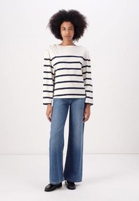 Stripete langermet topp i krem med marineblå striper, kombinert med vide blå denimjeans. Stoffet ser mykt og uformelt ut.