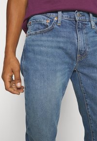 Jeans i medelblått denim med en slät yta, utrustade med koppardetaljer, sydda dekorationer och en figurnära design.