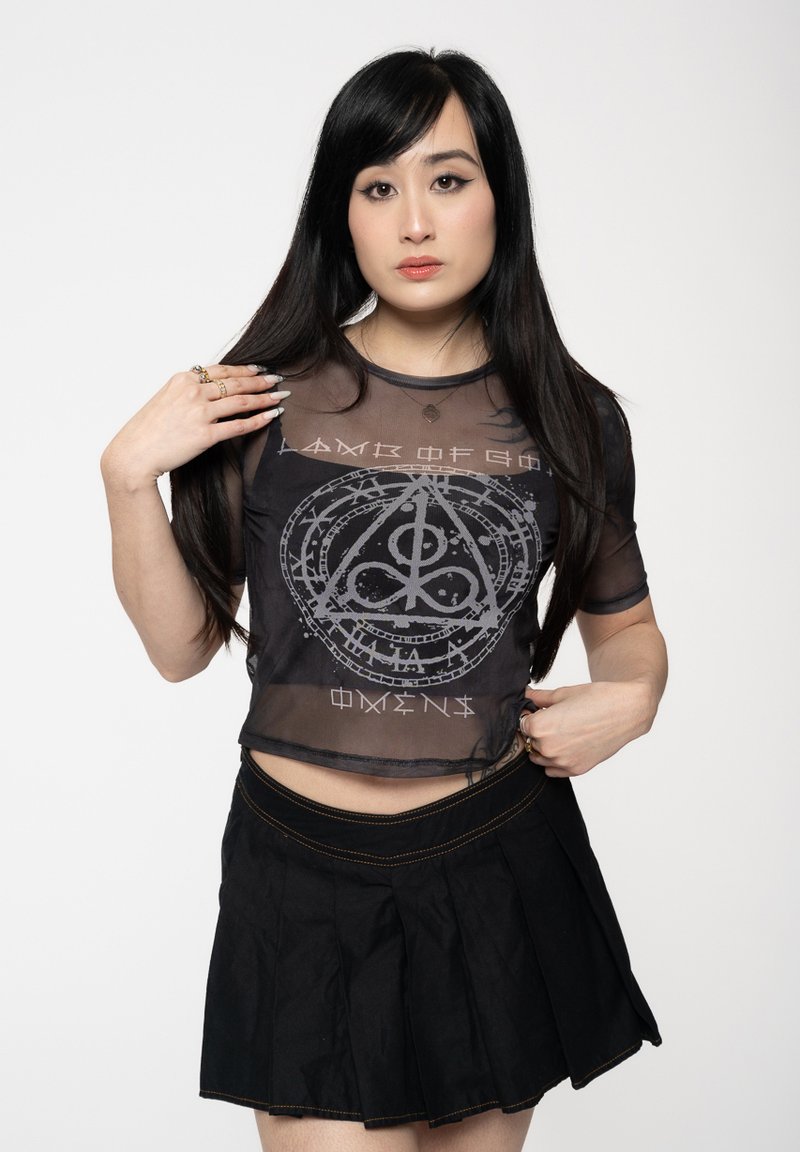 Black mesh crop top featuring a silver graphic design with intricate symbols, paired with a black pleated skirt with visible stitching details.
