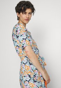 Vestido floral em azul-escuro com flores laranjas, rosas e verdes. Mangas curtas, cintura com laço e tecido suave com detalhes de impressão visíveis.