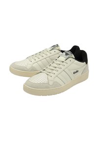 Sneaker color crema con punteggiature sulla punta, dettagli in suede, tre strisce laterali e tallone nero. Logo visibile sulla linguetta.