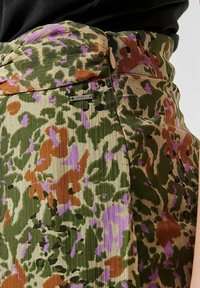 Jupe à motif floral dans les tons verts, marron et violets. Présente une texture côtelée et une taille pliée avec une étiquette de marque en métal.