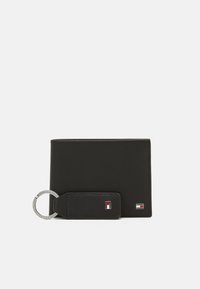 Portefeuille en cuir noir avec une texture lisse, doté d'une boucle de porte-clés et d'accents de logo en rouge et blanc. Conception rectangulaire compacte.