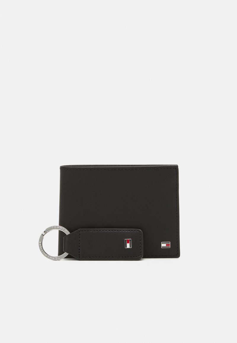 Portefeuille en cuir noir avec une texture lisse, doté d'une boucle de porte-clés et d'accents de logo en rouge et blanc. Conception rectangulaire compacte.
