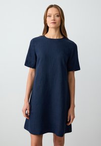 Navyblaues Leinenkleid mit Rundhalsausschnitt und kurzen Ärmeln, in lockerer Passform und knielanger Länge. Glatte Textur und minimales Design.