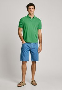 Green polo shirt, denim shorts, and brown sandals. Simple design, short sleeves, and relaxed fit. Smooth cotton texture and casual style.