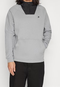 Felpa grigia con zip a quarto nera, tasca frontale e dettaglio del logo. Presenta una texture morbida e maniche raglan.