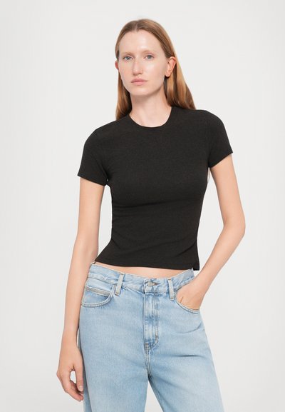 Black ribbed crop t-shirt with short sleeves, fitted design. Worn with light blue high-waisted jeans, featuring a button and pockets.