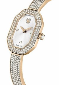 Oktagonalny zegarek z różowo-złotą metalową kopertą, srebrną tarczą i kryształowymi zdobieniami na bransolecie. Posiada dwa wskaźniki godzinowe oraz koronę.