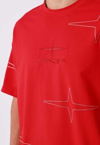 Rode T-shirt van zacht materiaal met een reliëflogo en sterontwerpen versierd met kleine strassteentjes. Korte mouwen, klassieke pasvorm.