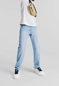 Vaqueros de mezclilla azul claro con corte recto, combinados con una camiseta blanca y un bolso cruzado marrón. Zapatillas en blanco y negro completan el look.