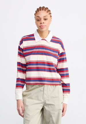 Gestreepte polo met lange mouwen in crème, rood en marineblauw met een witte kraag en een voorzakje; gemaakt van zachte katoen.