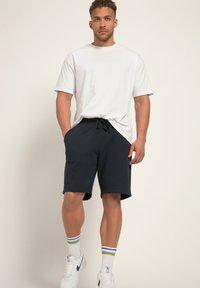 Herrenoutfit mit einem schlichten weißen Baumwoll-T-Shirt, marineblauen Shorts mit Kordelzug und weißen Sneakers mit mehrfarbigen gestreiften Socken.