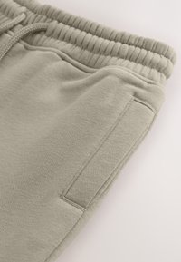Lichtbeige joggingbroek van zacht materiaal, met een geribde tailleband, trekkoord en een zijzak voor opbergruimte.