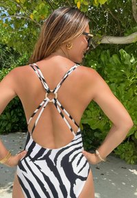 Zebra mintázatú, egyberészes fürdőruha, alacsony hátkivágással, keresztezett pántokkal és kör alakú fém kiegészítővel. Fekete és fehér színek.