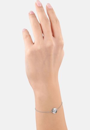 Bracciale d'argento con un ciondolo rotondo caratterizzato da un design a cuore testurizzato. Catena fine con una finitura liscia, indossato su una mano.