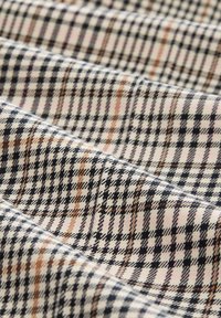 Tissu plié avec un fond beige et un motif à carreaux noir, marron et rose, montrant une texture douce et des détails fins de tissage.