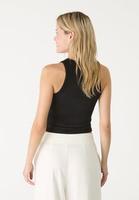 Černý crop top s přiléhavým střihem, bez rukávů a hladkým povrchem. Spárovaný s bílými kalhotami s vysokým pasem.