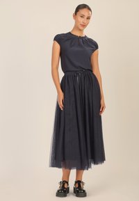 Vestido navy con mangas cortas abullonadas y un escote alto, acompañado de una falda de tul fluida y zapatos de plataforma negros. Detalles de diseño simples.