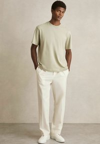 Tricou scurt cu mânecă în nuanță de măslin deschis, asortat cu pantaloni de culoare crem și adidași albi. Design simplu, textură netedă, croi relaxat.