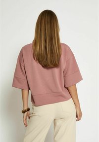 Felpa corta, a maniche corte, di colore rosa marrone, con una vestibilità morbida, caratterizzata da un'orlo arrotondato e una superficie liscia. Indossata con pantaloni chiari.