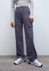 Grå cargo bukser i blødt stof med en løs pasform, med sidelommer og en knap i taljen, parret med hvide sneakers.