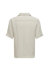 Short-sleeve, off-white shirt made of textured fabric with a collared neckline and back pleat detail. Minimalist design with no embellishments.