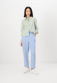 Grün-weiße gestreifte Button-Up-Bluse aus leichtem Stoff, kombiniert mit hellblauen, elastischen Hosen und weißen Sneakers.