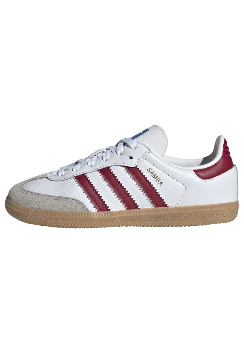 Chaussure de sport rétro blanche avec trois rayures zigzag maroon, capuchon en daim, semelle en caoutchouc, et étiquette de logo sur la languette.