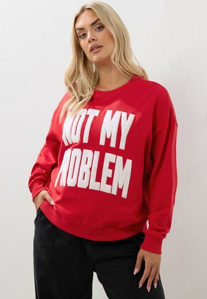 Sweatshirt rouge avec le texte texturé blanc "CE N'EST PAS MON PROBLÈME". Il dispose de manches longues, d'un col rond et d'une coupe décontractée.
