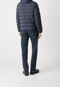 Navy puffer jacket with a quilted design, paired with dark denim jeans and black buckle shoes. Features a hood and standard cut.