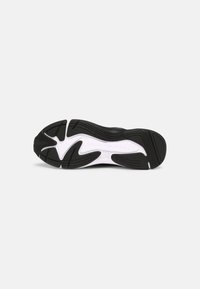 Semelle de chaussure de sport noire avec des accents blancs, présentant des motifs texturés pour une meilleure adhérence et un design courbé pour la flexibilité. Logo de la marque visible.