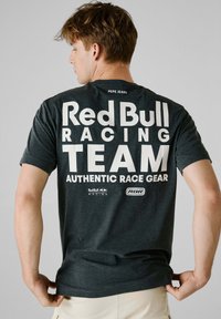 Mørkegrå t-shirt lavet af bomuld med korte ærmer. På ryggen står der med store hvide bogstaver: "Red Bull Racing TEAM AUTHENTIC RACE GEAR."