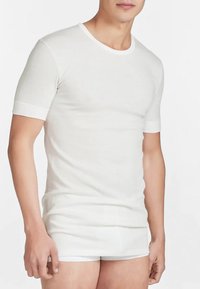 T-shirt bianco a maniche corte realizzato in tessuto morbido, con collo rotondo e design aderente, abbinato a pantaloni corti bianchi, di texture leggera e liscia.