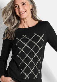 Schwarzes Langarmoberteil mit einem Kreuzmuster aus silbernen Pailletten auf der Vorderseite. Weichem Stoff mit Rundhalsausschnitt.