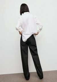Camisa blanca de botones con mangas arremangadas combinada con pantalones de pierna ancha negros. La tela suave y el corte relajado realzan la silueta general.