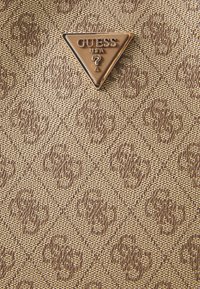 Brunt mønstret stof med hævede diamantformer har et trekantet guld "GUESS USA" logo i midten. Tekstureret og syntetisk materiale.