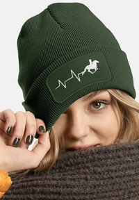 Dark green knitted beanie featuring a rectangular patch with a white equestrian silhouette and heartbeat line design. Soft texture.