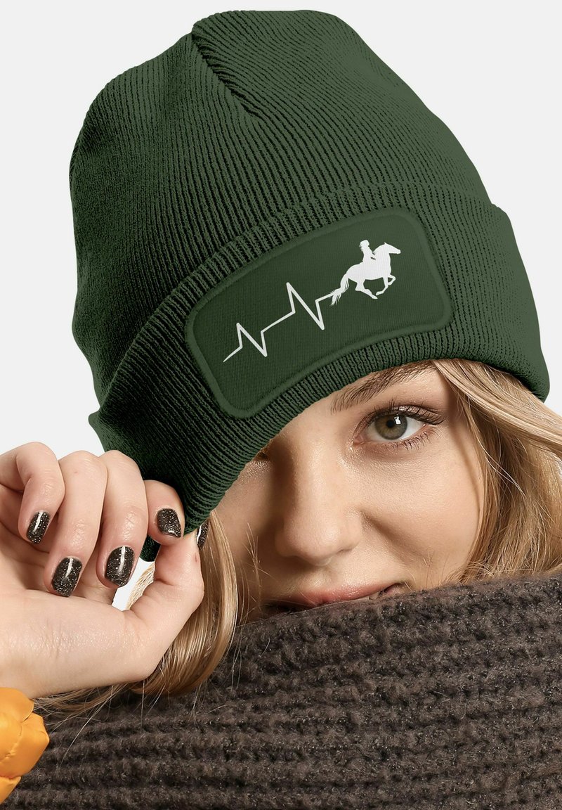Dark green knitted beanie featuring a rectangular patch with a white equestrian silhouette and heartbeat line design. Soft texture.