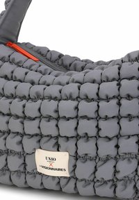 Borsa grigia in stile pochette realizzata in tessuto imbottito con una texture trapuntata. Presenta una cerniera arancione e una targhetta in metallo con il logo sulla parte anteriore.