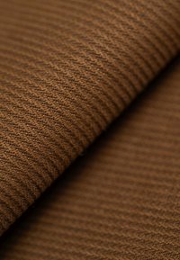 Brown textured fabric with a ribbed pattern, showing grooves and depth. The surface is soft, with a consistent color and finish.