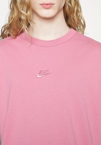 Rosa bomullströja med rundad halsringning och broderad Nike-logga på vänster bröst. Mjuk textur med en avslappnad passform.