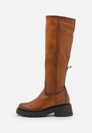 Bota alta de cuero marrón con suela gruesa negra y tiradores en la parte superior y trasera, vista lateral sobre fondo blanco.