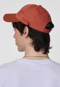 Justerbar röd kepp i bomull, med en b�öjd skärm, en ton-i-ton logotyp och ventilationshål. Baksidan är säkrad med ett rem.