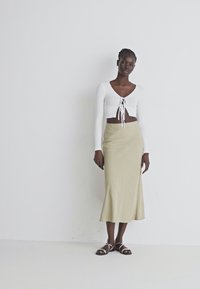White long-sleeve, cropped top with a tie-front detail paired with a form-fitting, knee-length olive green skirt and strappy sandals.